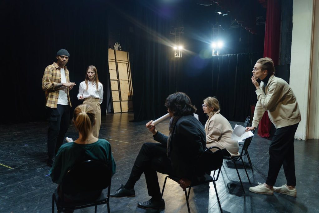 Actors rehearsing on stage with directors guidance in a theater for a live performance.