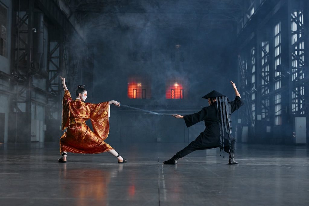 Two cosplayers in an intense martial arts face-off in a dramatic industrial setting.
